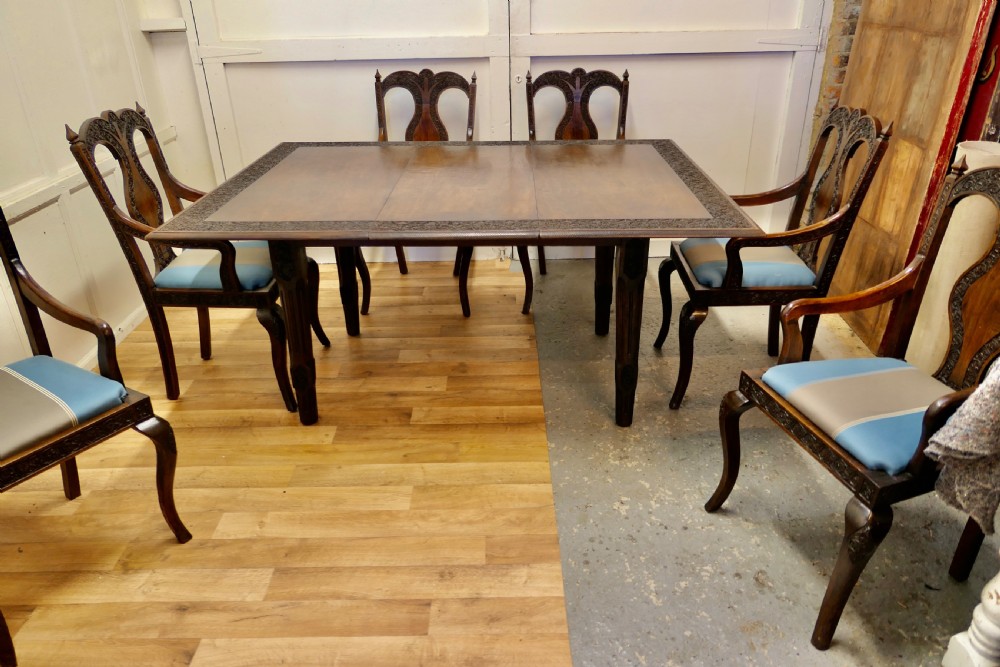 A dark wood rectangular dining table with a carved relief border surrounded by six matching carved wooden chairs with light blue striped upholstered seat pads. View VII