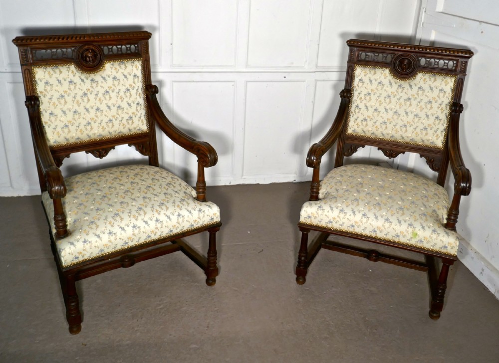 A pair of carved dark wood French Gothic armchair thrones with floral upholstered backrests and seats.