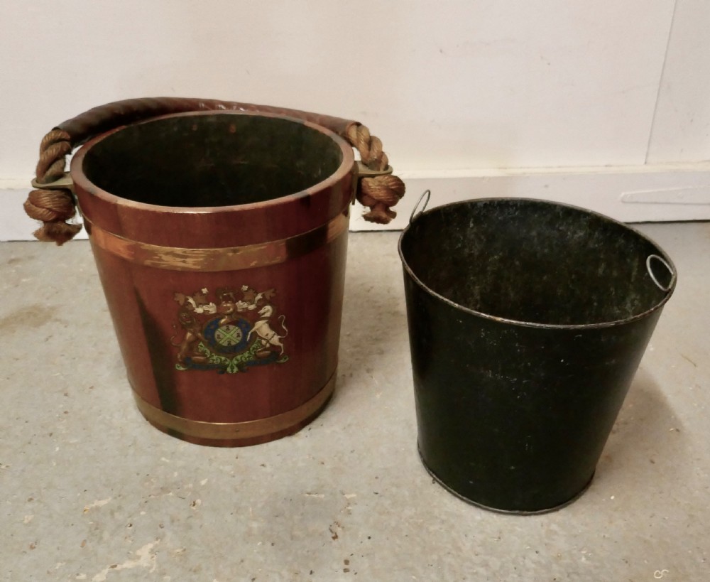 A 19th-century dark oak fire bucket featuring brass binding, a thick rope handle covered in brown leather, and a painted Plymouth armorial crest on the front. View VII