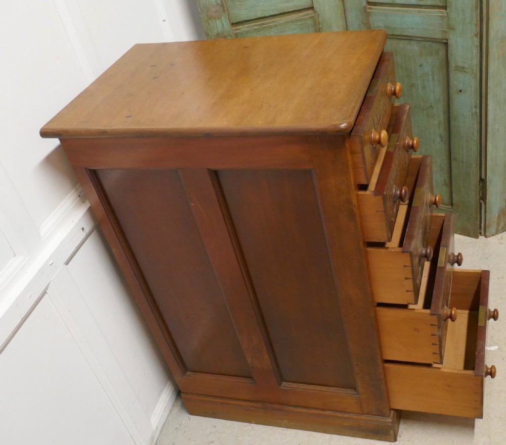 A tall Victorian pine chest featuring five drawers with turned wooden knobs and hand-painted gilt pharmacy lettering across each drawer front. View V