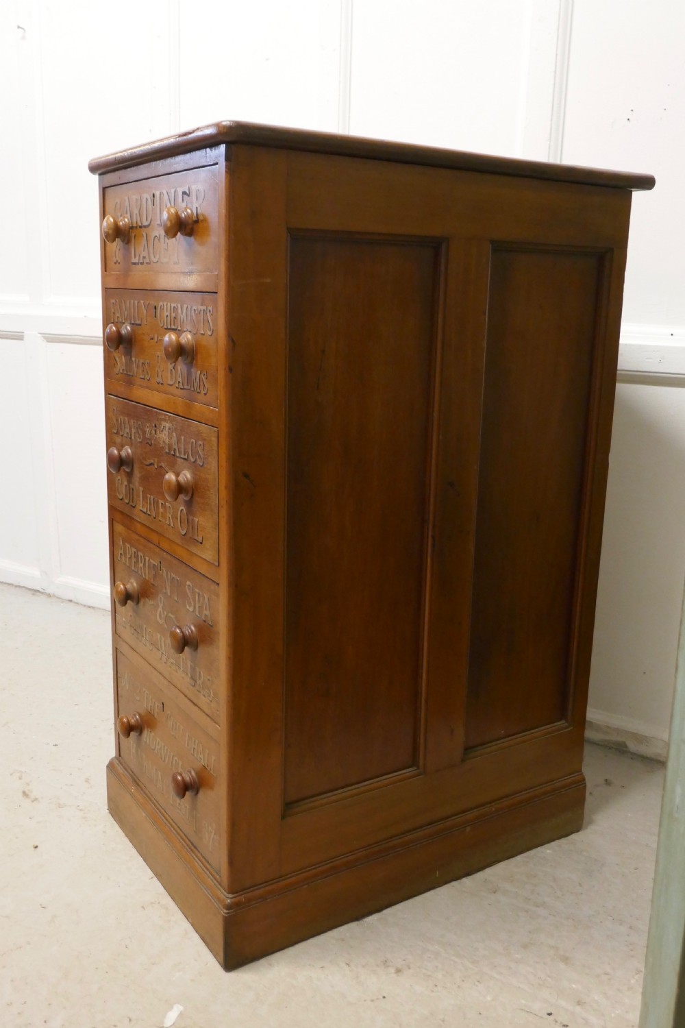 A tall Victorian pine chest featuring five drawers with turned wooden knobs and hand-painted gilt pharmacy lettering across each drawer front. View XVI