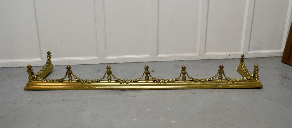 A 19th-century brass fireplace fender curb featuring baluster posts with pinecone finials and cast brass floral garlands.