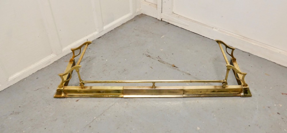 A polished Art Nouveau brass fireplace fender featuring sinuous openwork side supports and a central low horizontal rail. View II