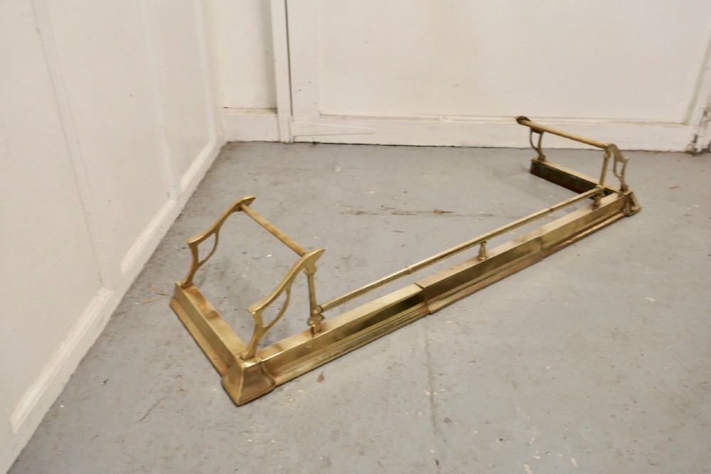 A polished Art Nouveau brass fireplace fender featuring sinuous openwork side supports and a central low horizontal rail. View III