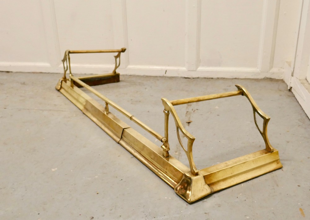 A polished Art Nouveau brass fireplace fender featuring sinuous openwork side supports and a central low horizontal rail. View IV