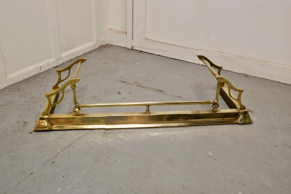 A polished Art Nouveau brass fireplace fender featuring sinuous openwork side supports and a central low horizontal rail. View V