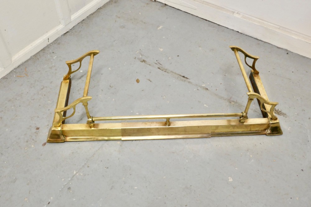 A polished Art Nouveau brass fireplace fender featuring sinuous openwork side supports and a central low horizontal rail. View VI