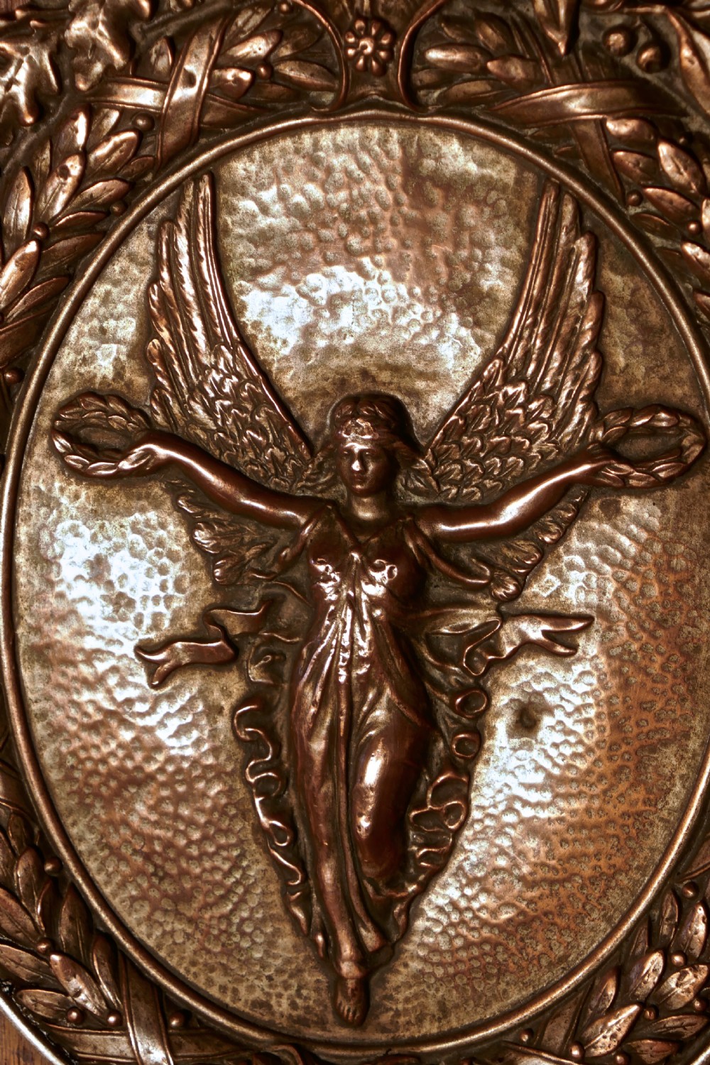An oval oak wooden plaque featuring a copper relief medallion depicting the winged goddess Nike surrounded by a laurel wreath. View II
