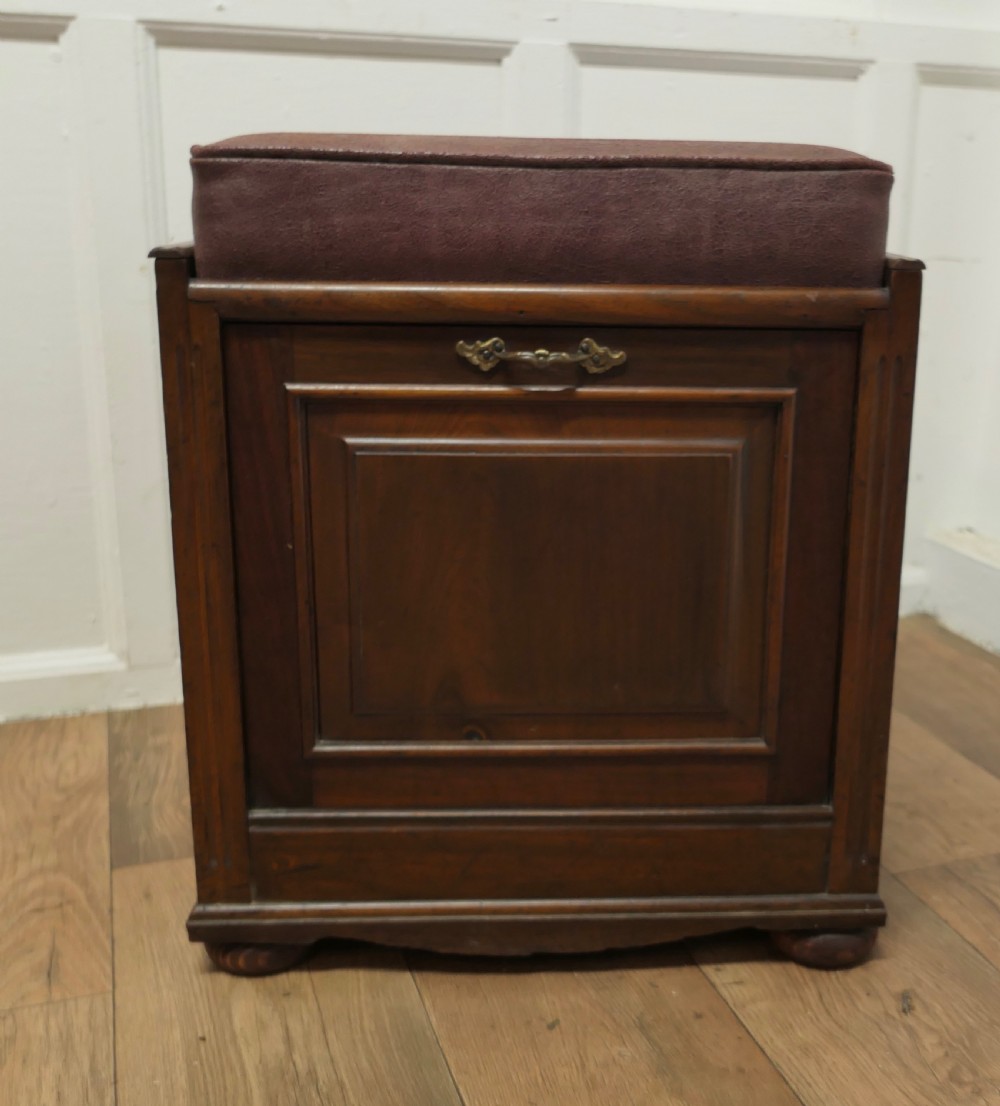 A dark walnut Victorian piano stool featuring a deep cushioned seat, moulded front fall panel, and a central brass drop handle.