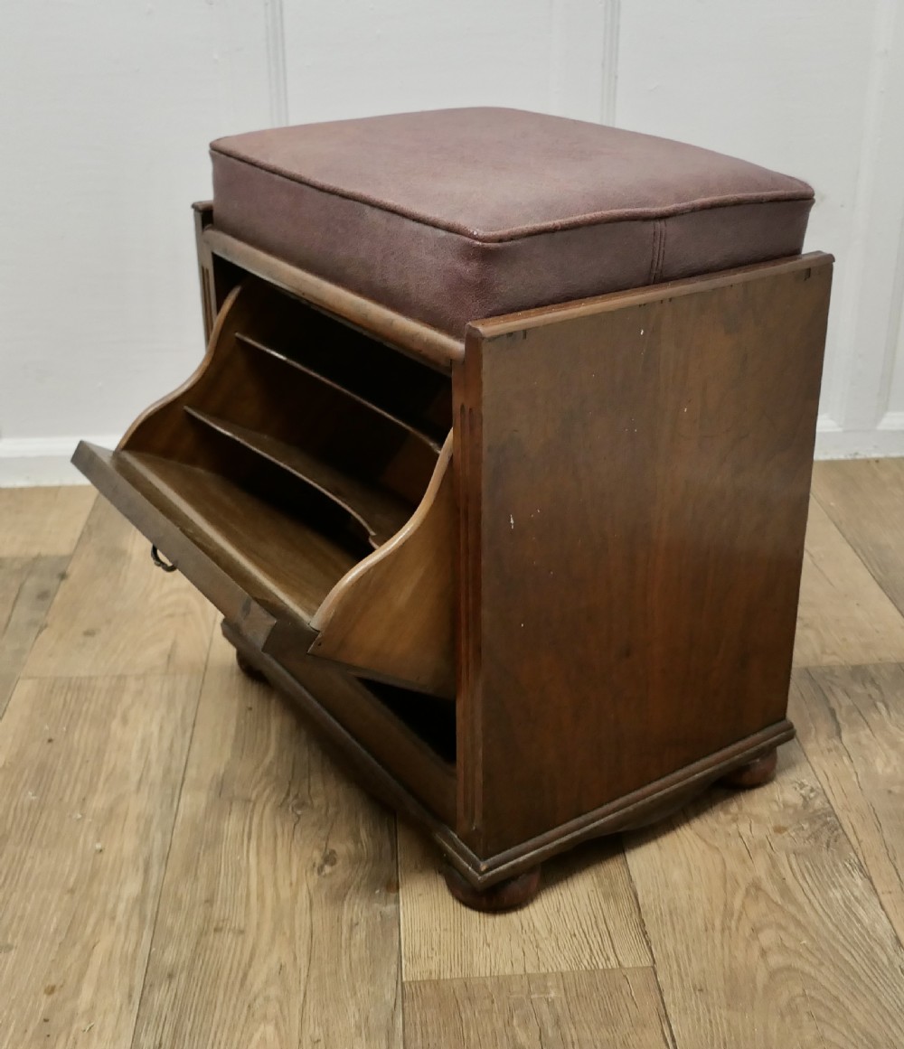 A dark walnut Victorian piano stool featuring a deep cushioned seat, moulded front fall panel, and a central brass drop handle. View VI