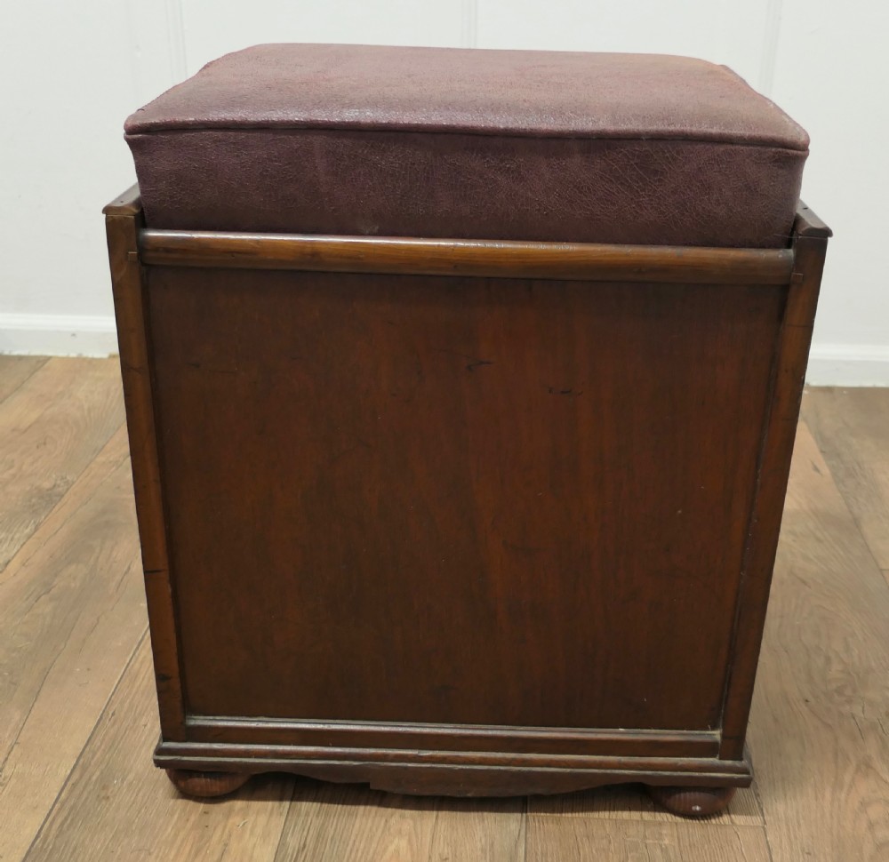 A dark walnut Victorian piano stool featuring a deep cushioned seat, moulded front fall panel, and a central brass drop handle. View VII