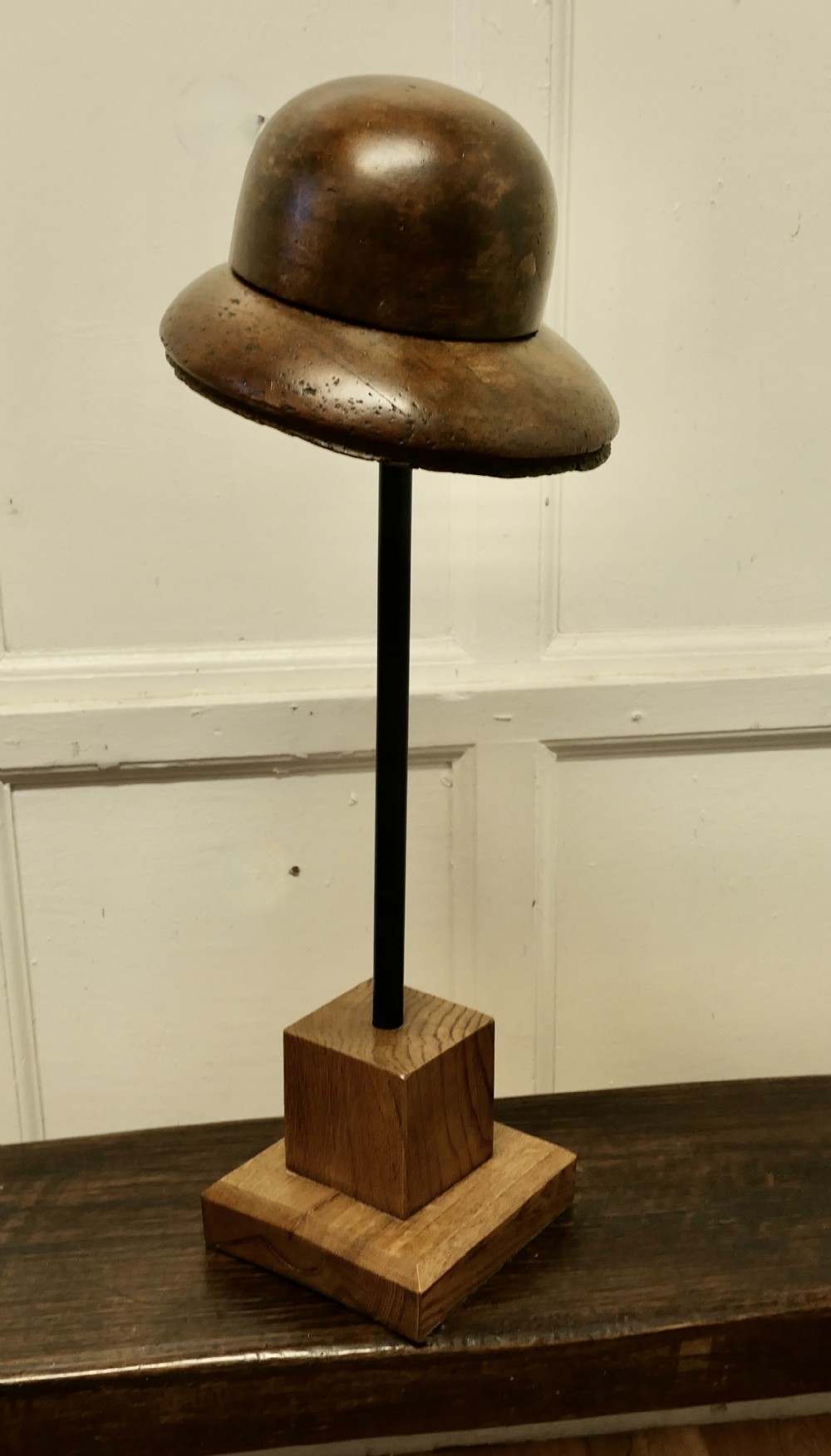 An antique French fruitwood hat display stand featuring a carved wooden crown form mounted on a black metal shaft with a wooden base.