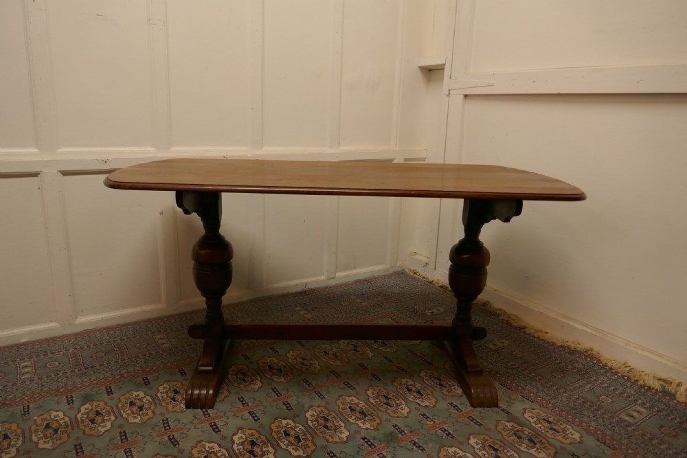 A solid warm brown oak refectory dining table featuring turned baluster supports connected by a low central stretcher base.