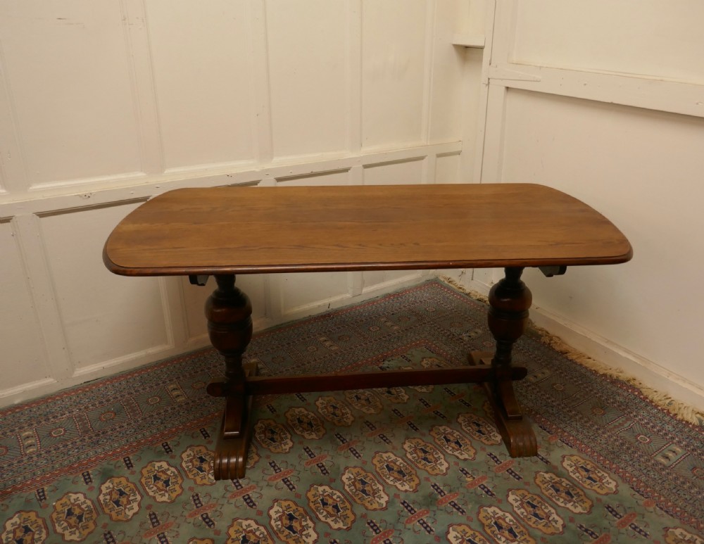 A solid warm brown oak refectory dining table featuring turned baluster supports connected by a low central stretcher base. View II