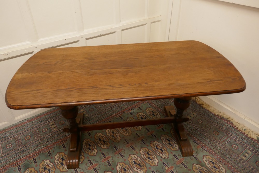 A solid warm brown oak refectory dining table featuring turned baluster supports connected by a low central stretcher base. View III