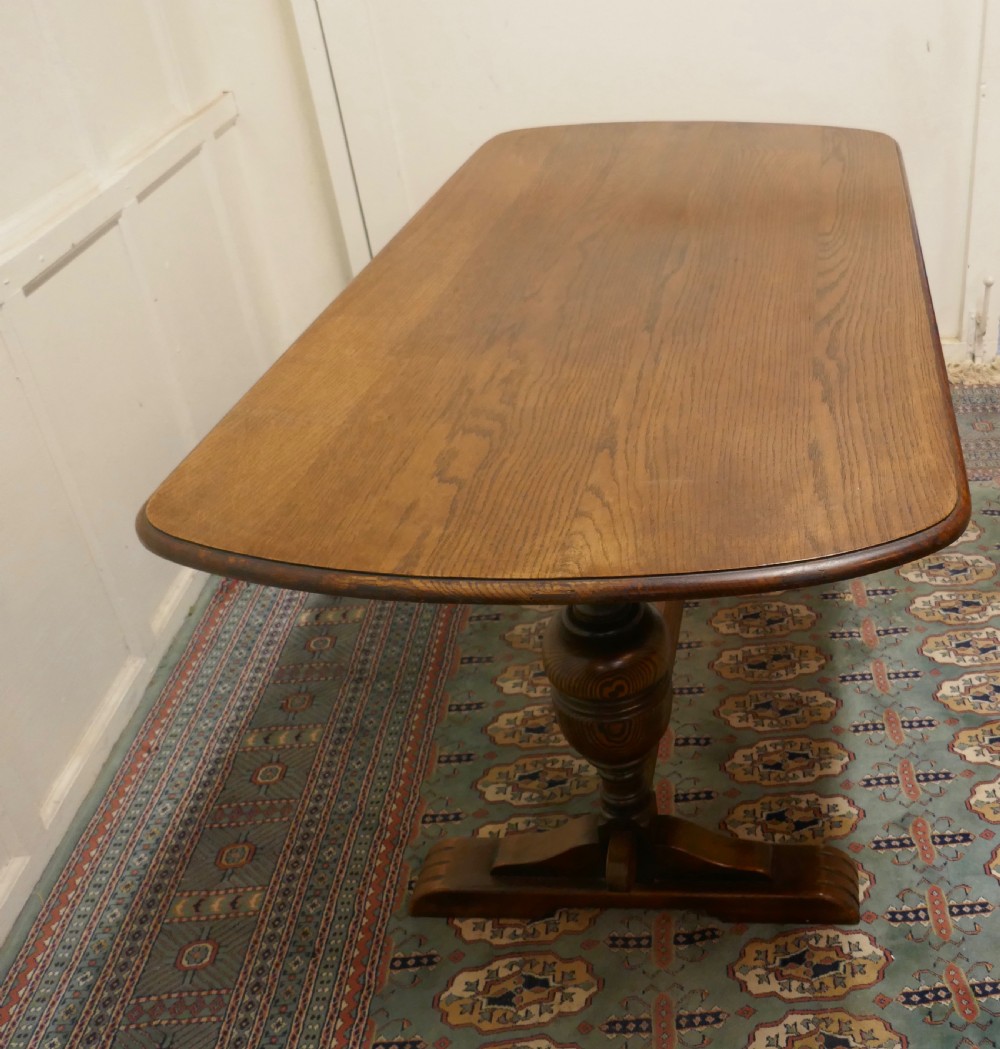 A solid warm brown oak refectory dining table featuring turned baluster supports connected by a low central stretcher base. View V