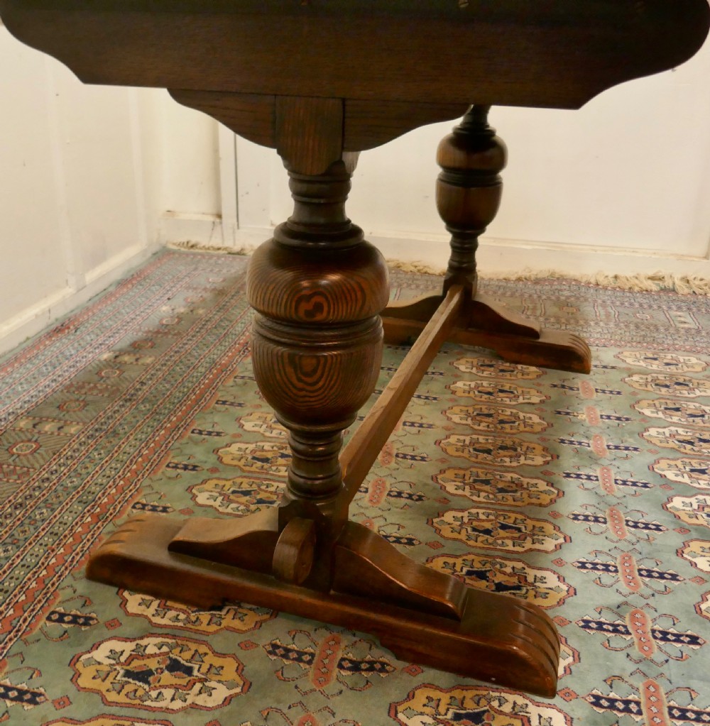 A solid warm brown oak refectory dining table featuring turned baluster supports connected by a low central stretcher base. View VI