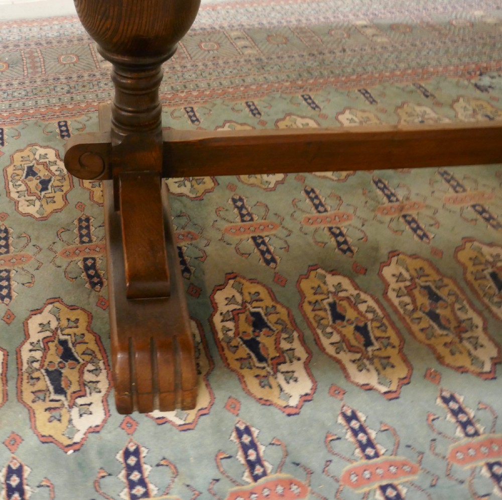 A solid warm brown oak refectory dining table featuring turned baluster supports connected by a low central stretcher base. View VII