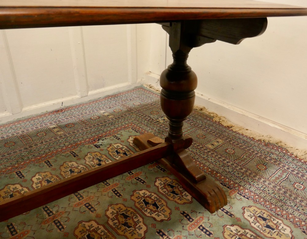 A solid warm brown oak refectory dining table featuring turned baluster supports connected by a low central stretcher base. View VIII