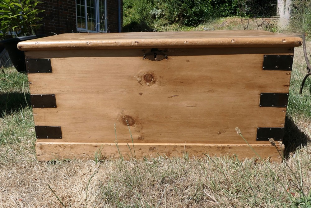 A rectangular stripped pine blanket box with dark iron corner brackets, a keyhole escutcheon, and a flat hinged lid.
