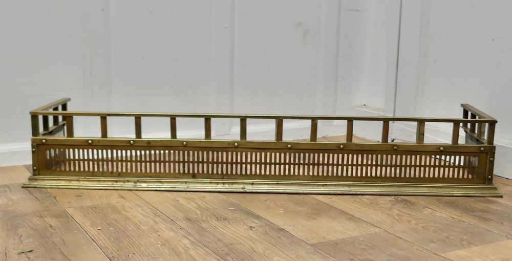 A Victorian solid brass fireplace fender featuring a slotted lower gallery, stud detailing, and an elevated top rail.