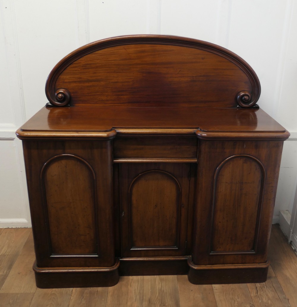 A Victorian mahogany sideboard featuring a large arched scroll backboard over a recessed central cupboard door flanked by panelled side cupboards on a plinth base. View II