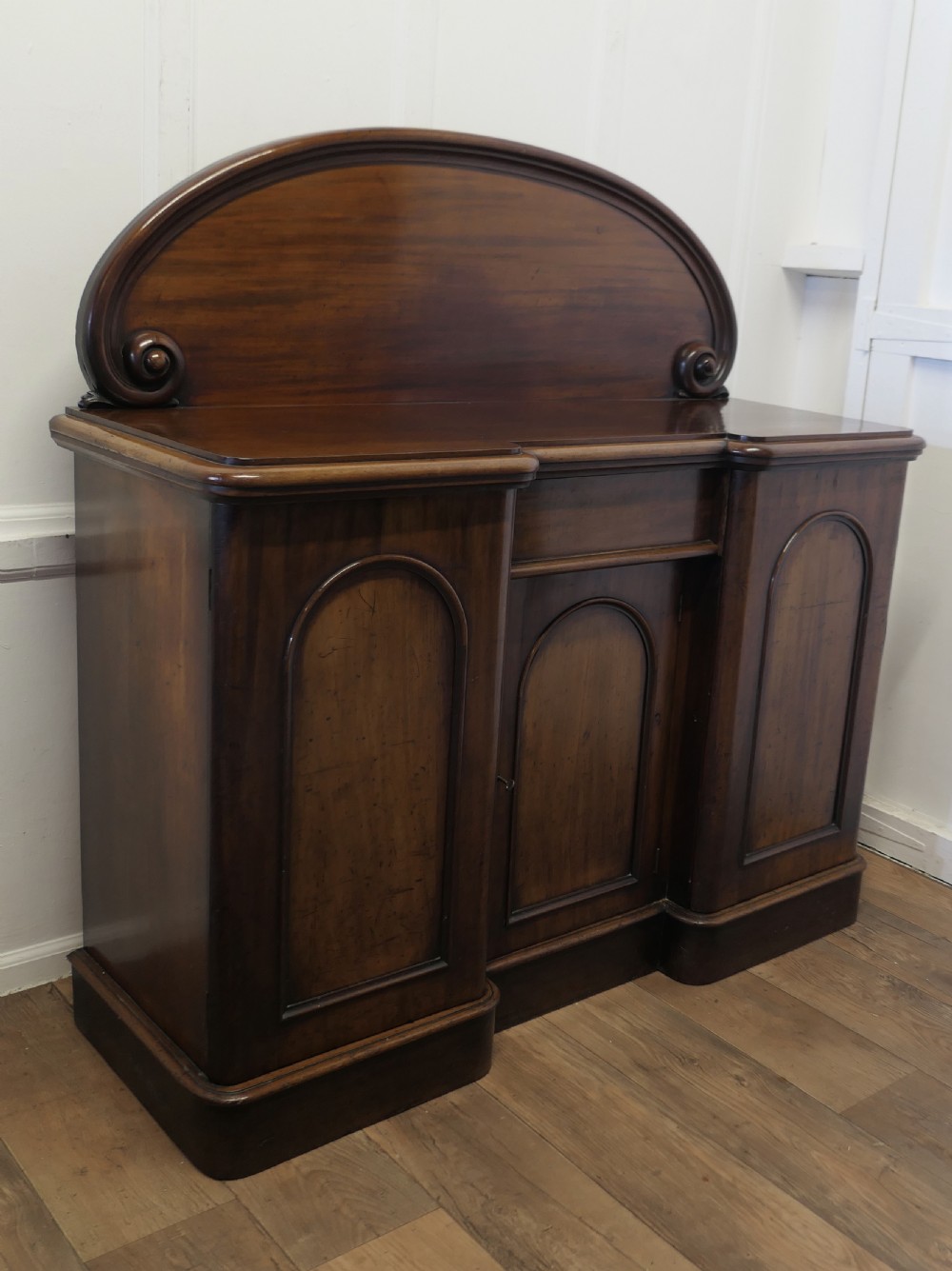 A Victorian mahogany sideboard featuring a large arched scroll backboard over a recessed central cupboard door flanked by panelled side cupboards on a plinth base. View III