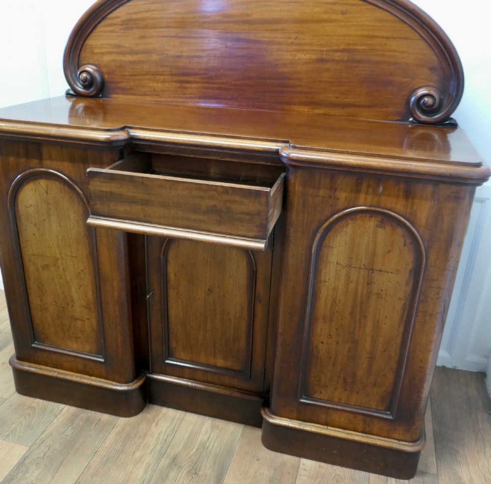 A Victorian mahogany sideboard featuring a large arched scroll backboard over a recessed central cupboard door flanked by panelled side cupboards on a plinth base. View VII