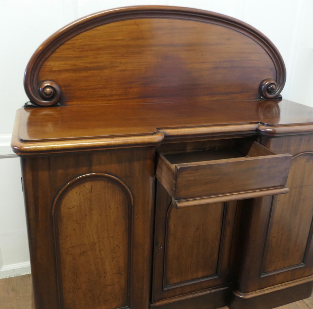 A Victorian mahogany sideboard featuring a large arched scroll backboard over a recessed central cupboard door flanked by panelled side cupboards on a plinth base. View VIII