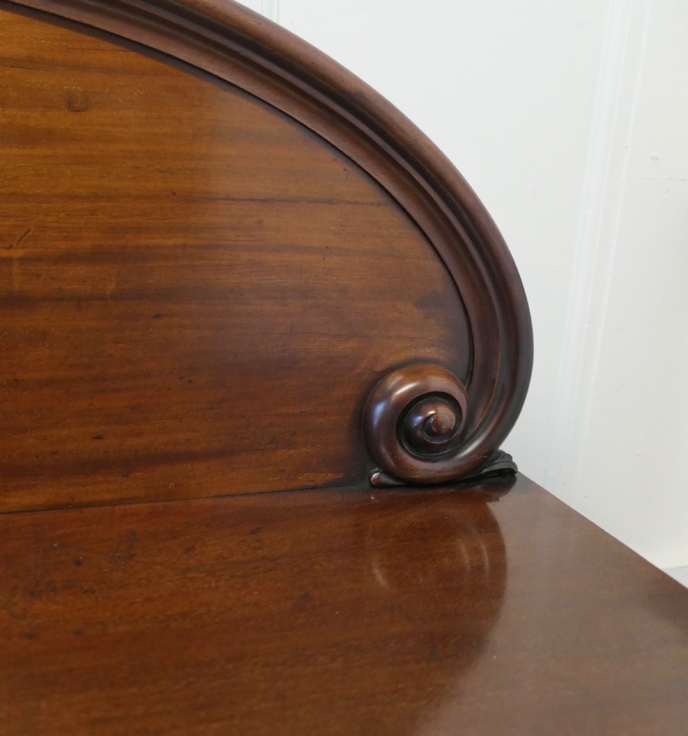 A Victorian mahogany sideboard featuring a large arched scroll backboard over a recessed central cupboard door flanked by panelled side cupboards on a plinth base. View XI