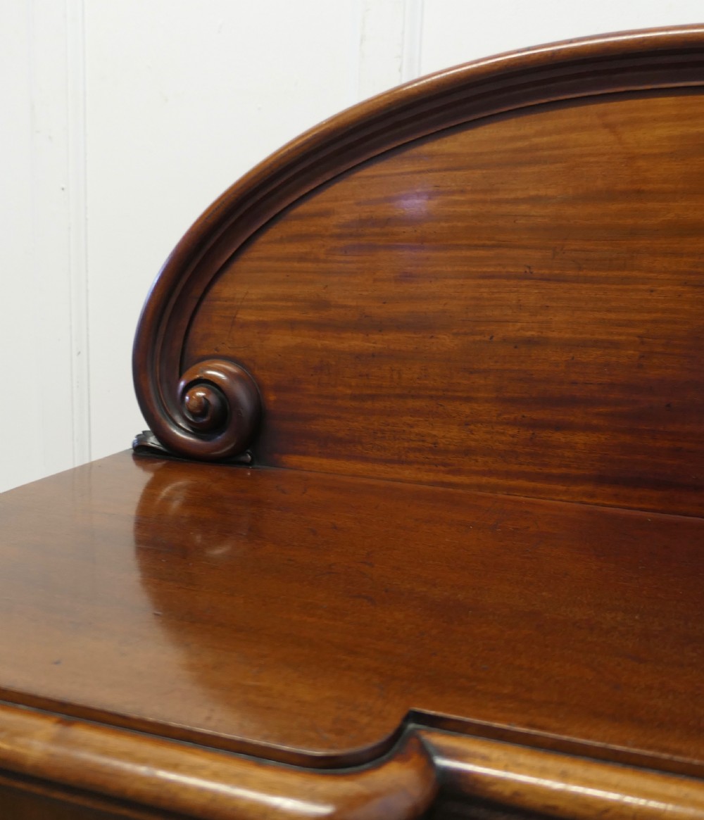 A Victorian mahogany sideboard featuring a large arched scroll backboard over a recessed central cupboard door flanked by panelled side cupboards on a plinth base. View XII