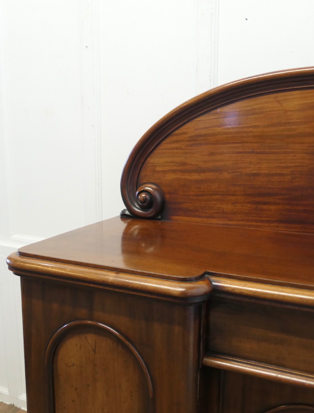 A Victorian mahogany sideboard featuring a large arched scroll backboard over a recessed central cupboard door flanked by panelled side cupboards on a plinth base. View XIII