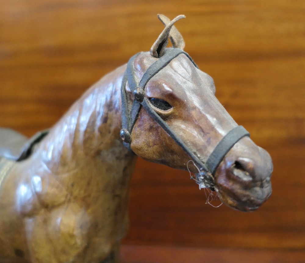 A handcrafted brown leather model of a horse featuring a miniature dark leather saddle, harness, and brass stirrup loops. View III