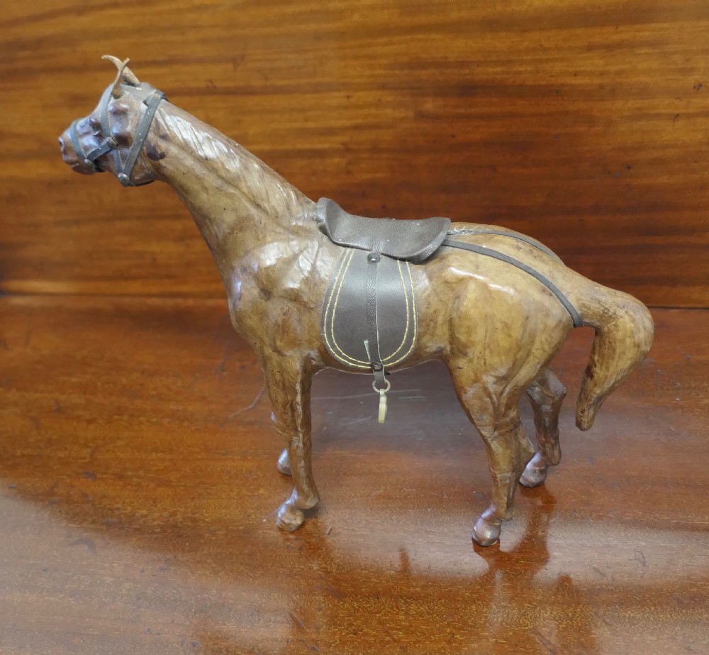 A handcrafted brown leather model of a horse featuring a miniature dark leather saddle, harness, and brass stirrup loops. View IV