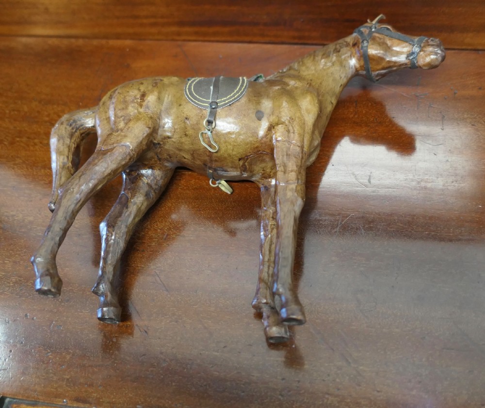 A handcrafted brown leather model of a horse featuring a miniature dark leather saddle, harness, and brass stirrup loops. View VI