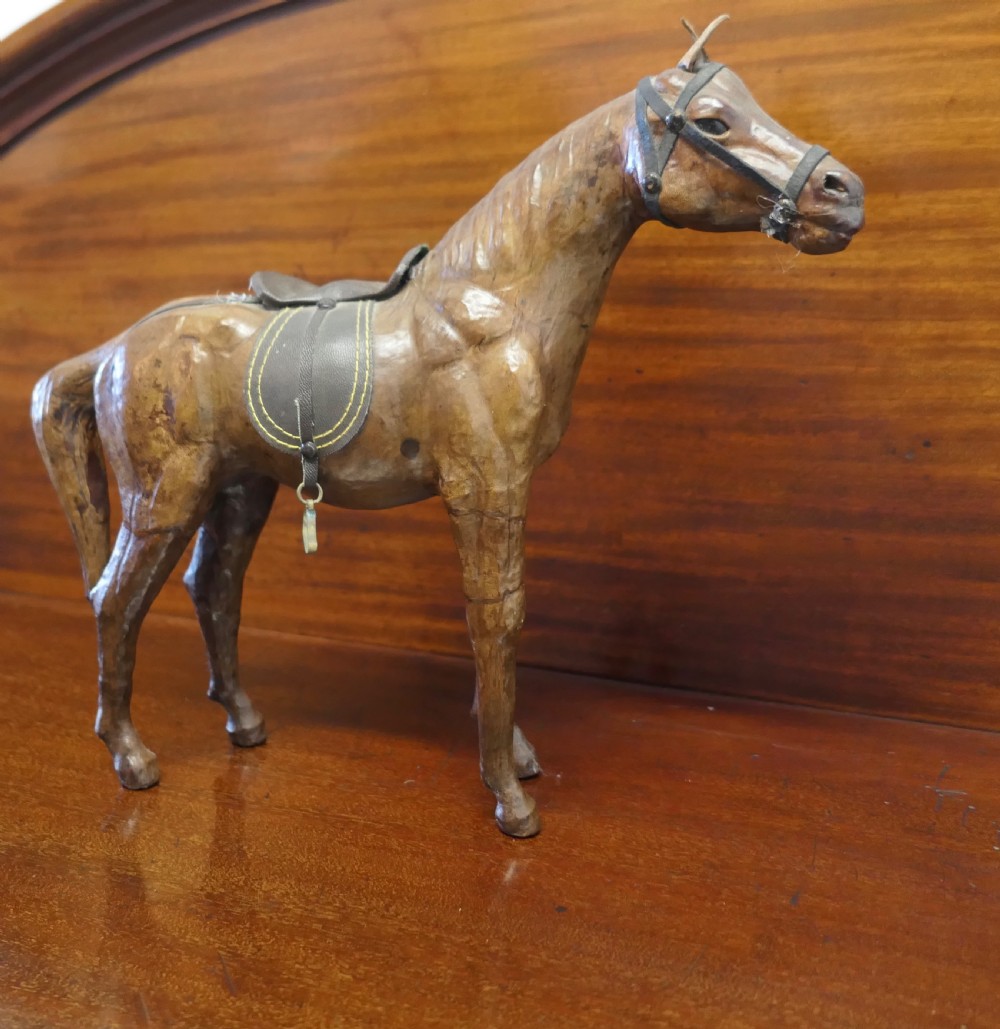 A handcrafted brown leather model of a horse featuring a miniature dark leather saddle, harness, and brass stirrup loops. View VIII