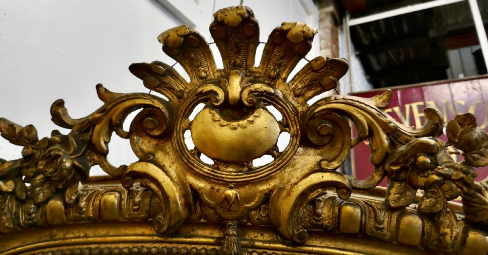 A large 19th-century French arched giltwood wall mirror featuring an ornate carved cresting pediment and beaded border. View VIII