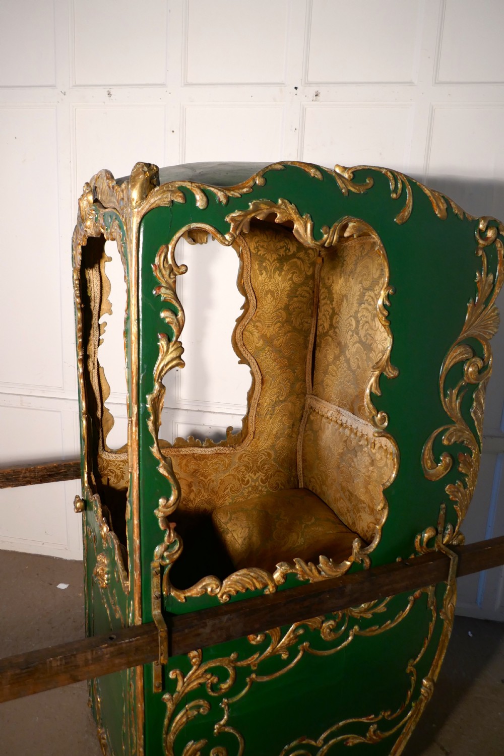A 19th-century green painted and giltwood Italian sedan chair featuring hand-carved scrollwork, window openings, gold fabric lining, and wooden carrying poles. View II
