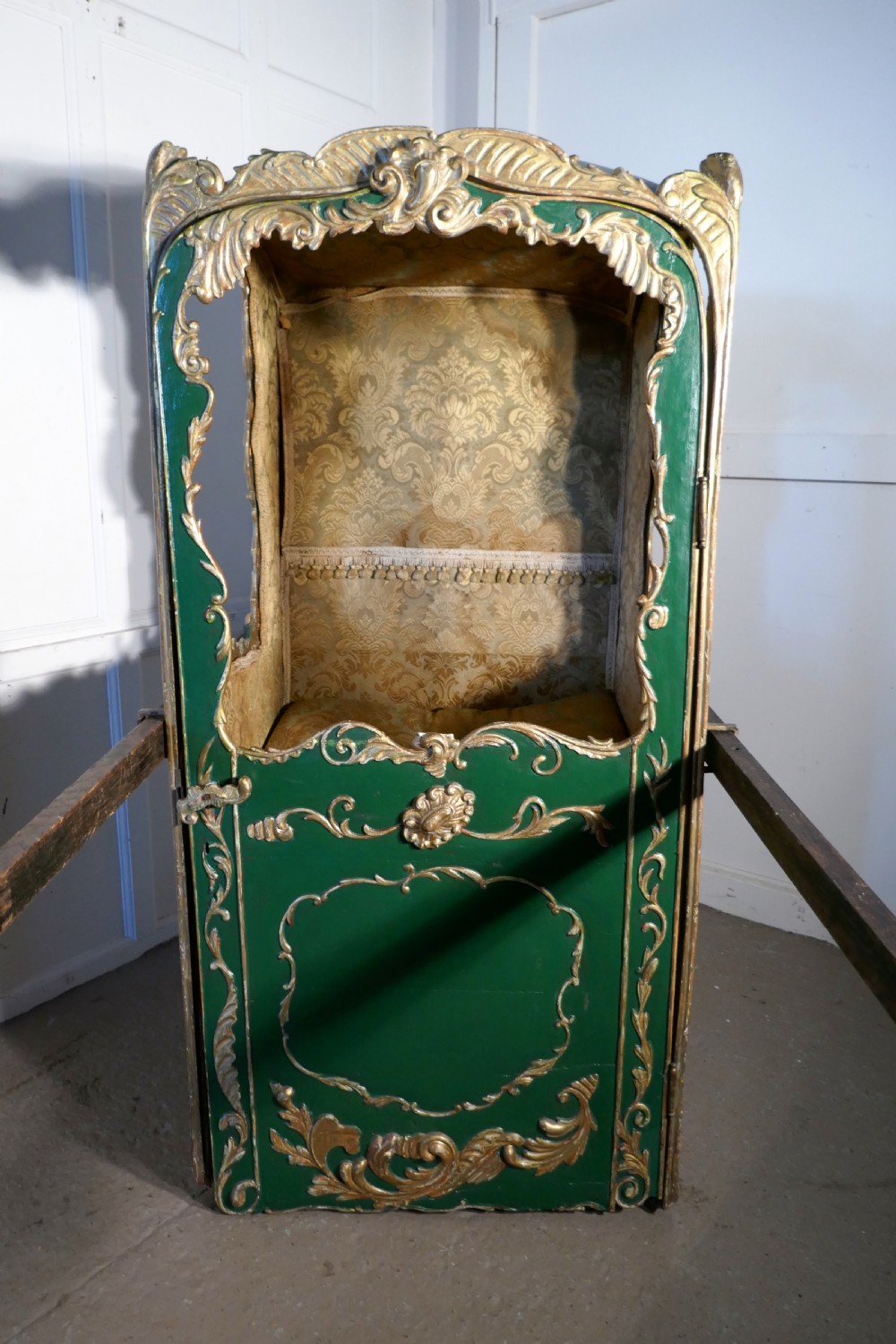 A 19th-century green painted and giltwood Italian sedan chair featuring hand-carved scrollwork, window openings, gold fabric lining, and wooden carrying poles. View III