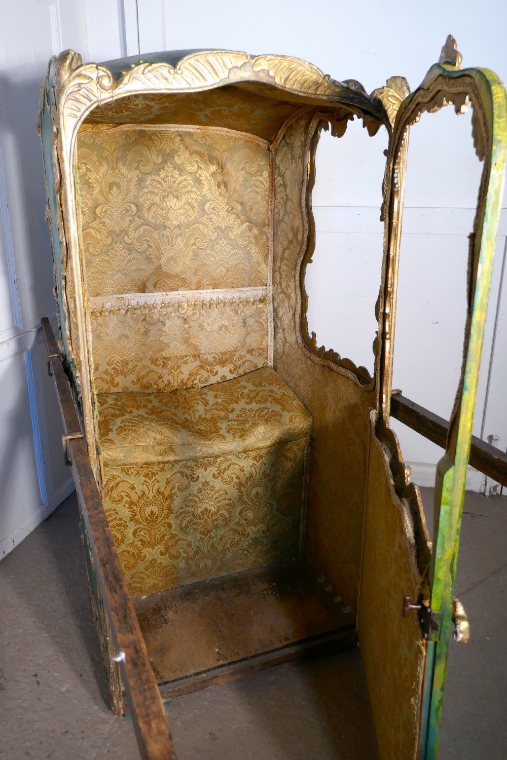 A 19th-century green painted and giltwood Italian sedan chair featuring hand-carved scrollwork, window openings, gold fabric lining, and wooden carrying poles. View IV