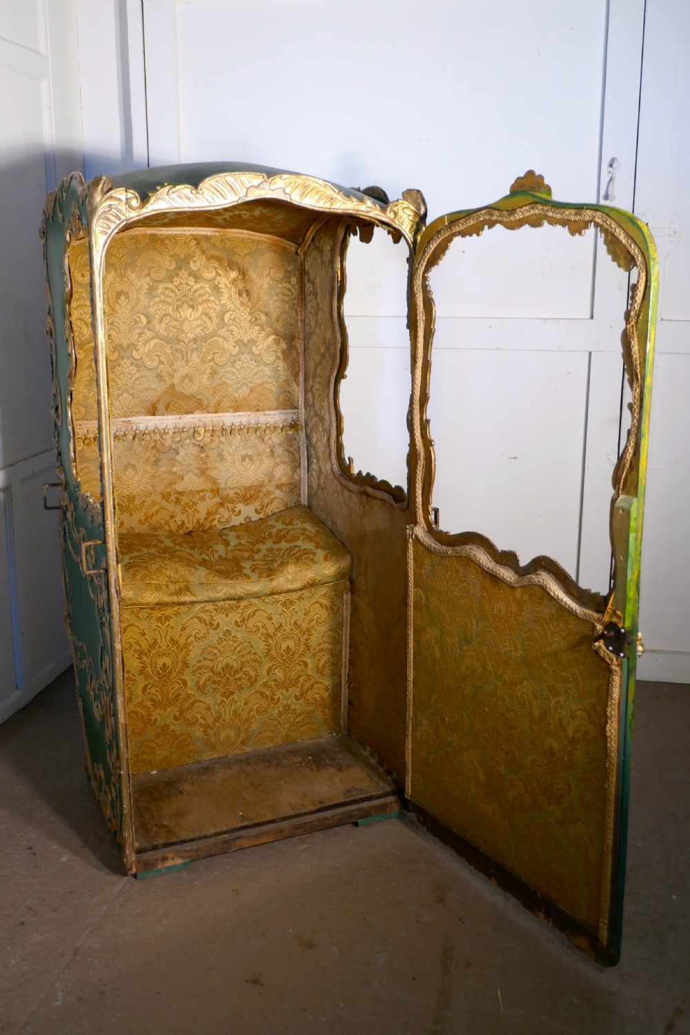 A 19th-century green painted and giltwood Italian sedan chair featuring hand-carved scrollwork, window openings, gold fabric lining, and wooden carrying poles. View VI