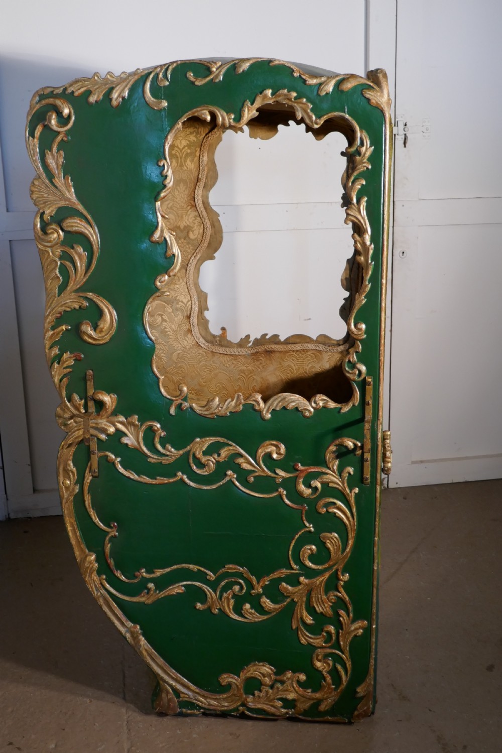 A 19th-century green painted and giltwood Italian sedan chair featuring hand-carved scrollwork, window openings, gold fabric lining, and wooden carrying poles. View VIII