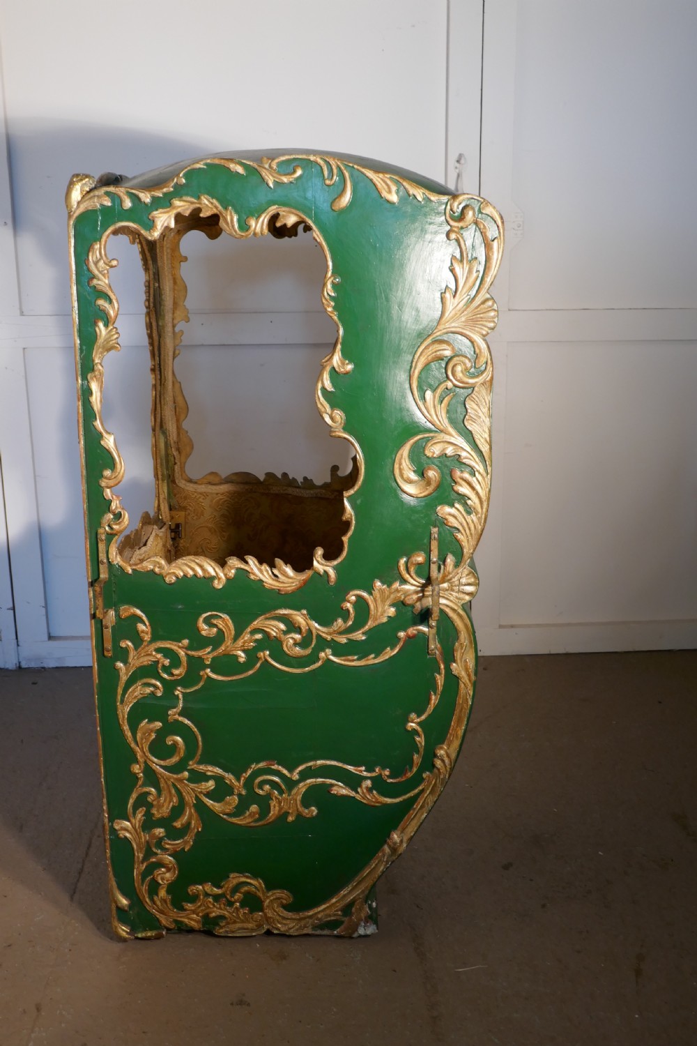 A 19th-century green painted and giltwood Italian sedan chair featuring hand-carved scrollwork, window openings, gold fabric lining, and wooden carrying poles. View XI