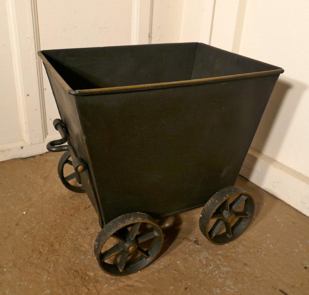 A dark iron coal scuttle shaped like a miniature wagon with four spoked wheels and a rear handle.