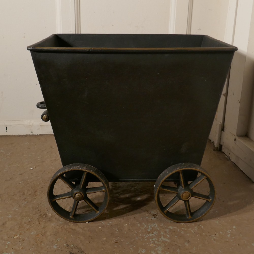 A dark iron coal scuttle shaped like a miniature wagon with four spoked wheels and a rear handle. View III