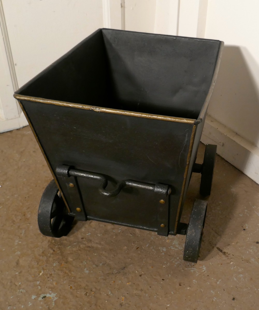 A dark iron coal scuttle shaped like a miniature wagon with four spoked wheels and a rear handle. View V