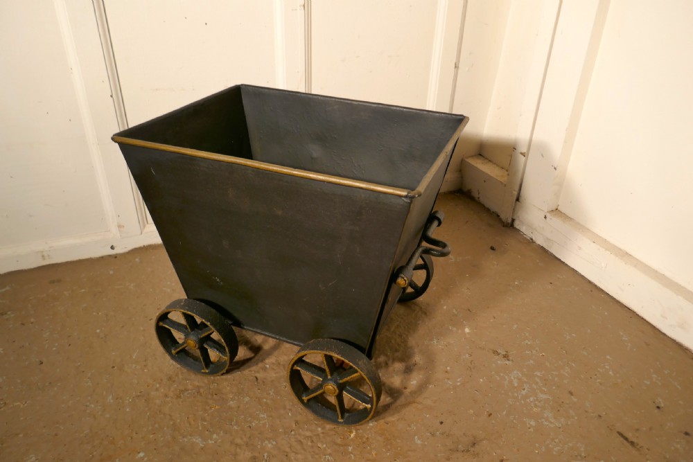 A dark iron coal scuttle shaped like a miniature wagon with four spoked wheels and a rear handle. View VI