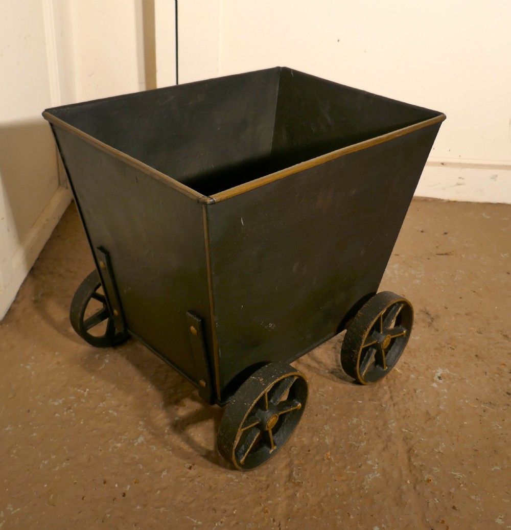 A dark iron coal scuttle shaped like a miniature wagon with four spoked wheels and a rear handle. View VII