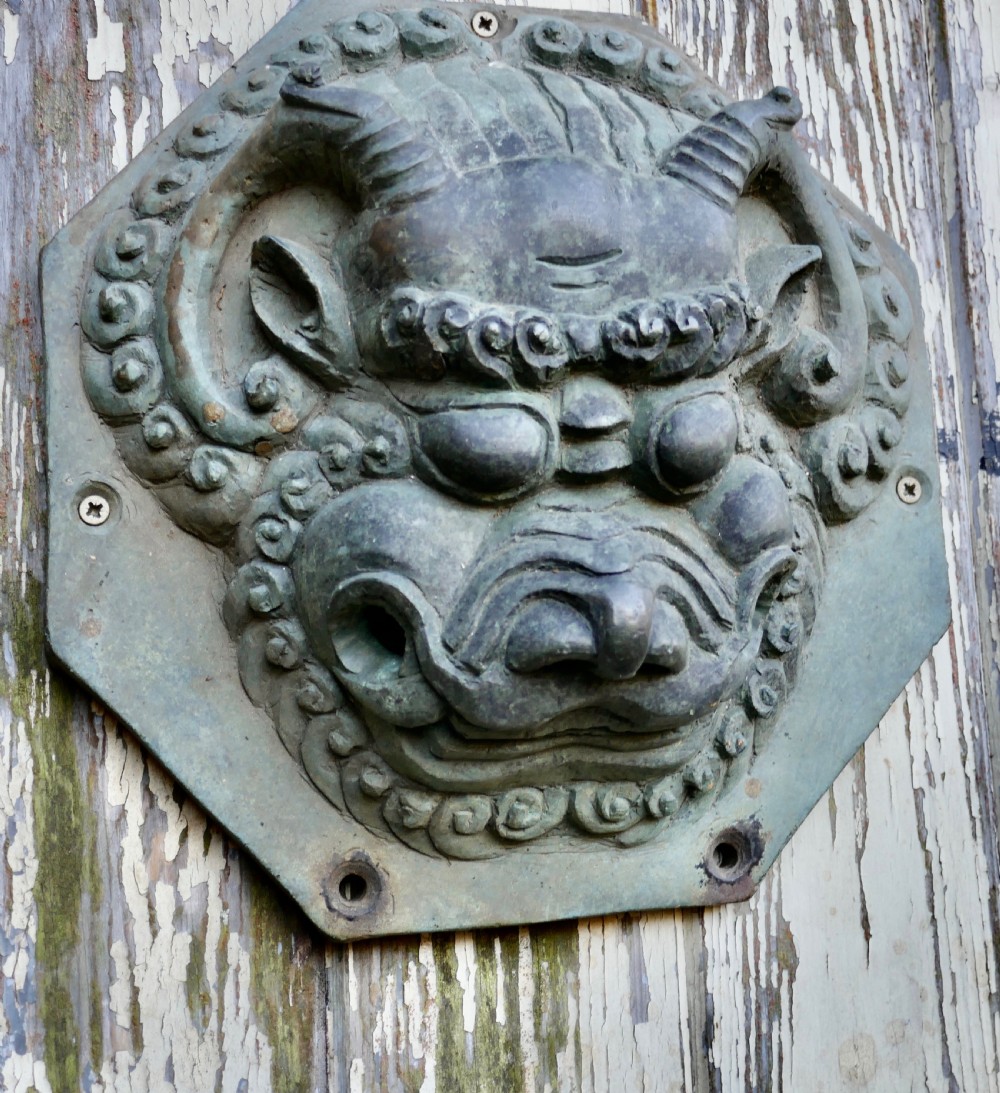 A pair of octagonal patinated bronze Chinese door plates featuring relief carvings of guardian lion heads with curled manes and horns. View V