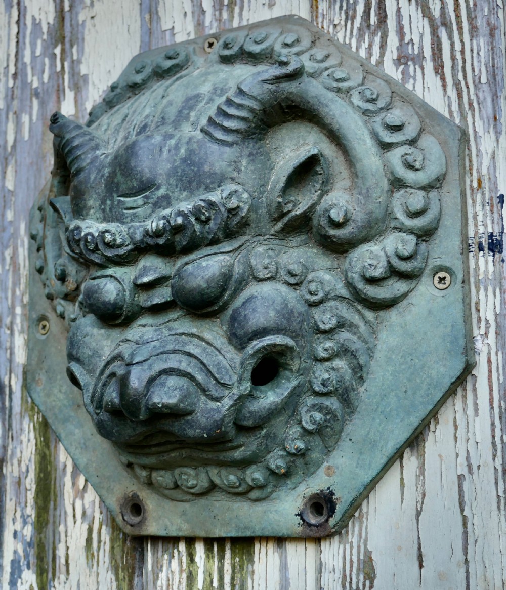 A pair of octagonal patinated bronze Chinese door plates featuring relief carvings of guardian lion heads with curled manes and horns. View VI